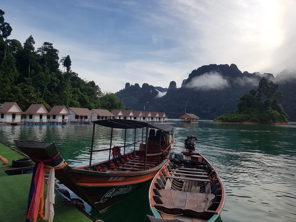 Longtail boats on water with floating huts and mountains in the background.