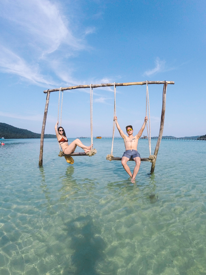 Two people on swings over water with distant islands.