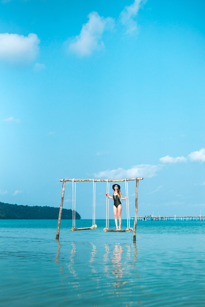 Woman on a swing over the sea with a bright blue sky.