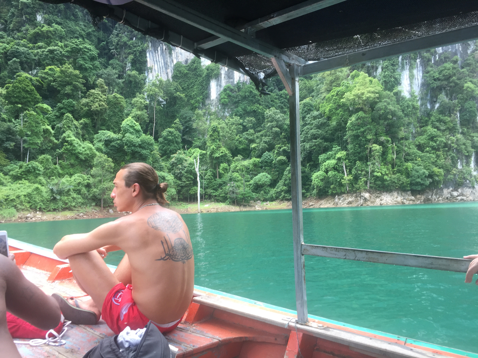 Person sitting at the edge of a boat surrounded by turquiose water and rainforest mountains.