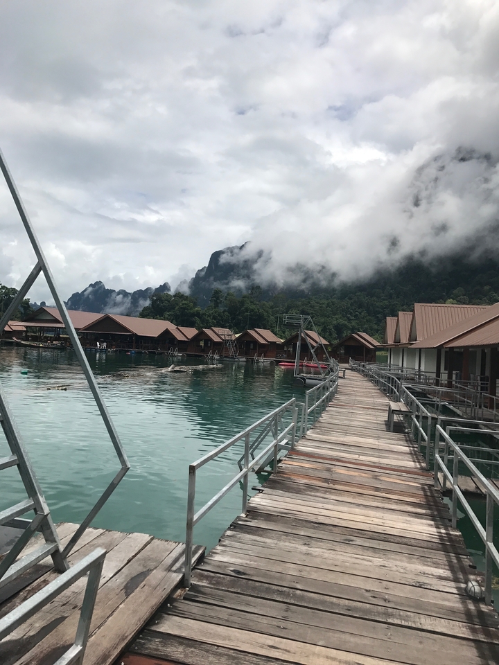 Floating wooden bungalows on a lake with mist-covered hills in the background.