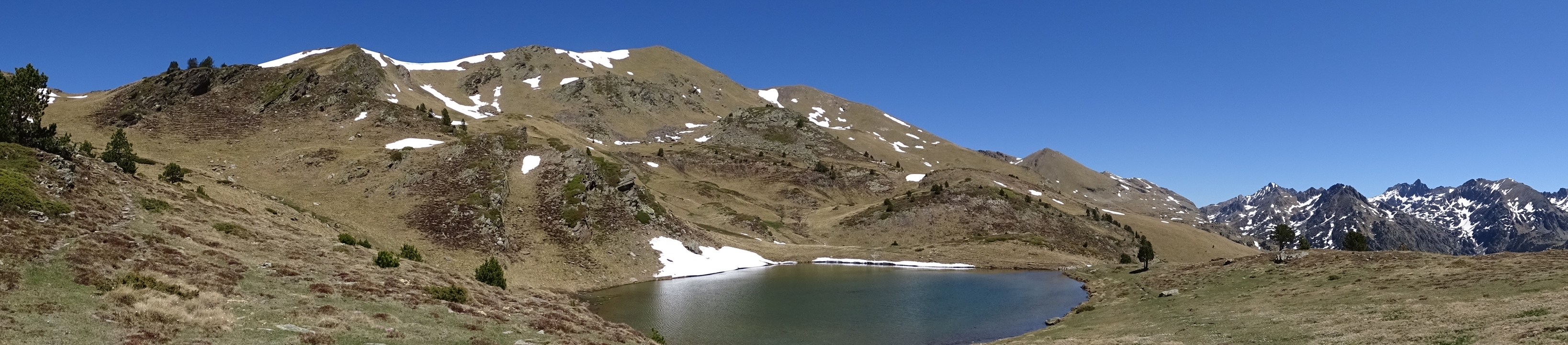Lac de montagne avec des plaques de neige environnantes sous un ciel bleu clair.