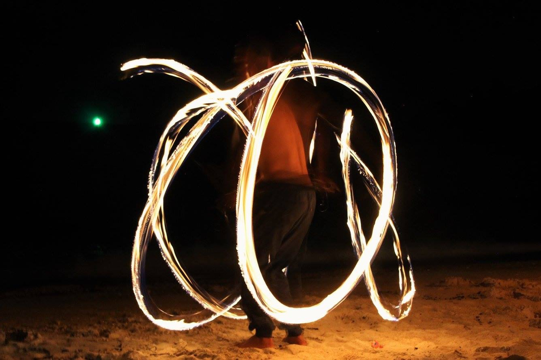 Performer spinning fire at night on a beach.