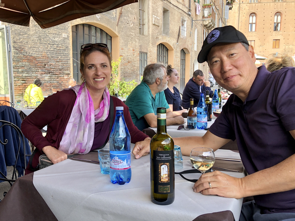 People dining at an outdoor restaurant table with wine.