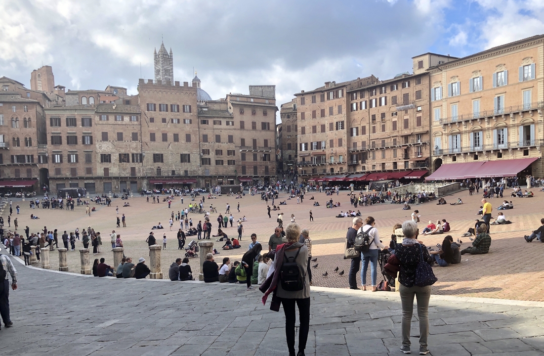 Piazza with people sitting and walking surrounded by historic architecture.