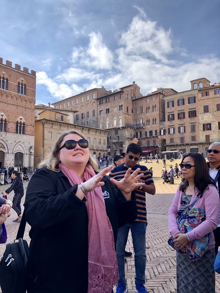 Tourist guide speaking to a group in a historic square with old buildings.