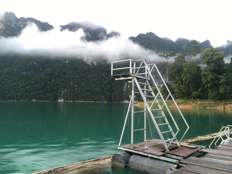 A metal diving platform by a still lake with a cloudy mountain backdrop.
