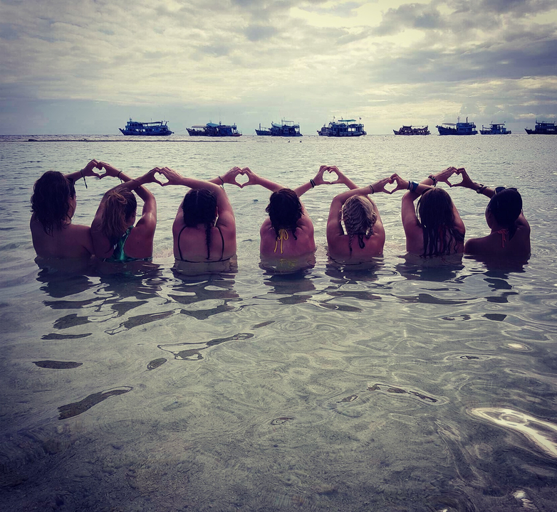 People standing in the water making heart shapes with their hands.