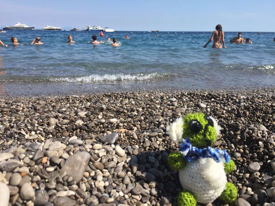 Plage de galets avec des gens qui se baignent et un petit jouet en peluche au premier plan.