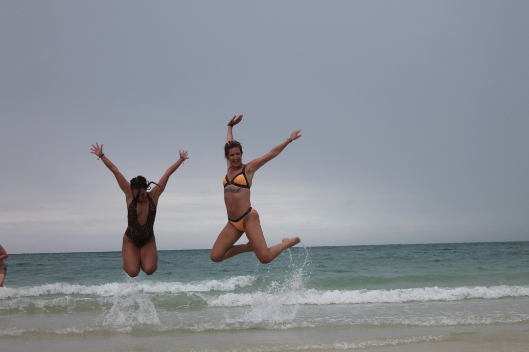 Deux personnes sautant sur une plage avec l'océan en arrière-plan.