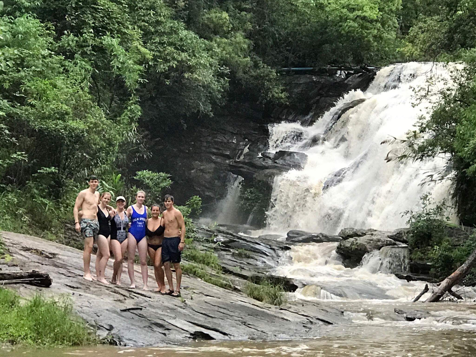 Group standing in front of a waterfall in a forest setting.