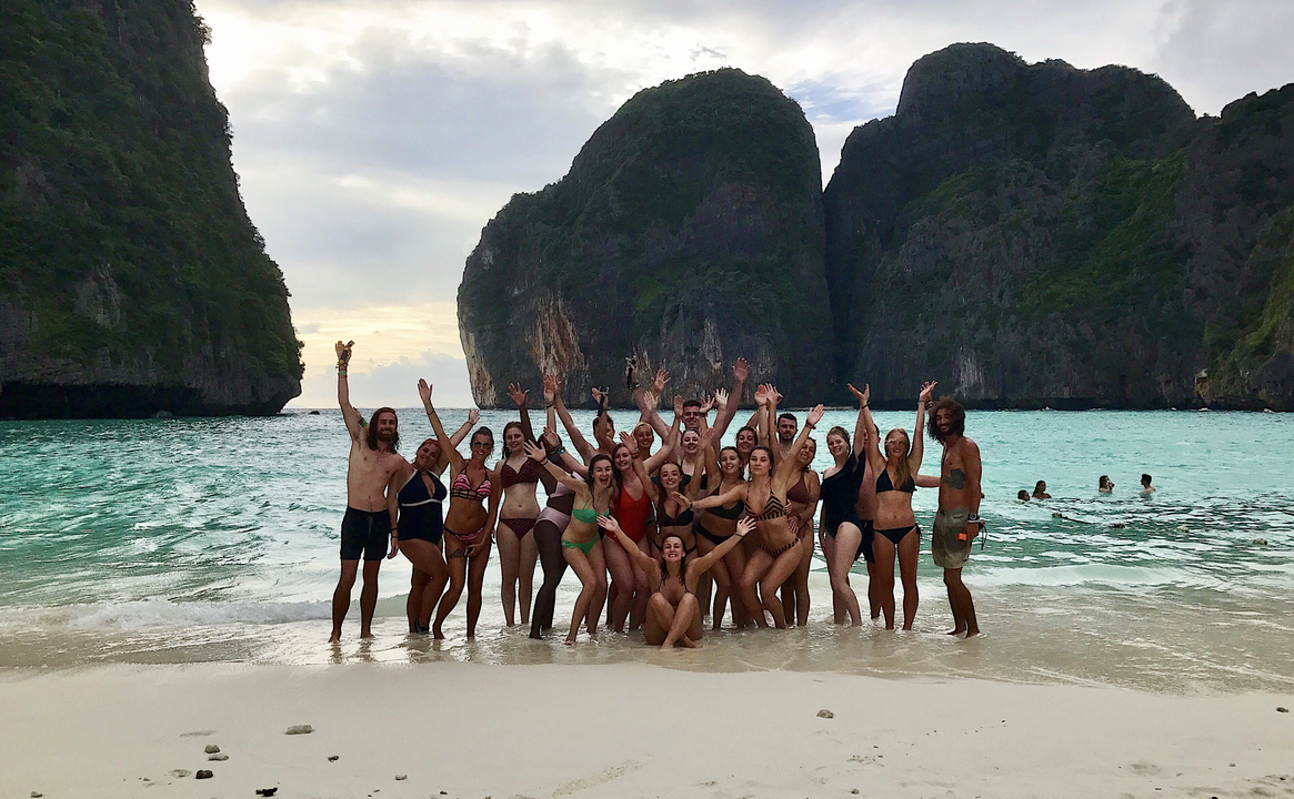 Group of people posing on a beach with scenic cliffs.