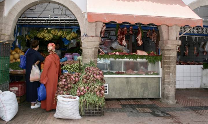 Market scene with people shopping for fresh produce and meats.