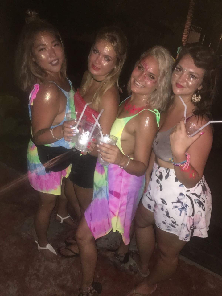 People holding drinks and wearing brightly colored clothing adorned with paint.