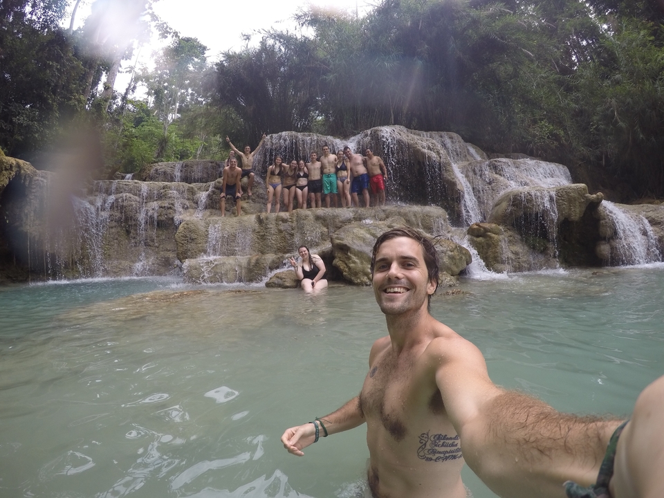 People posing by a waterfall in a forested area.