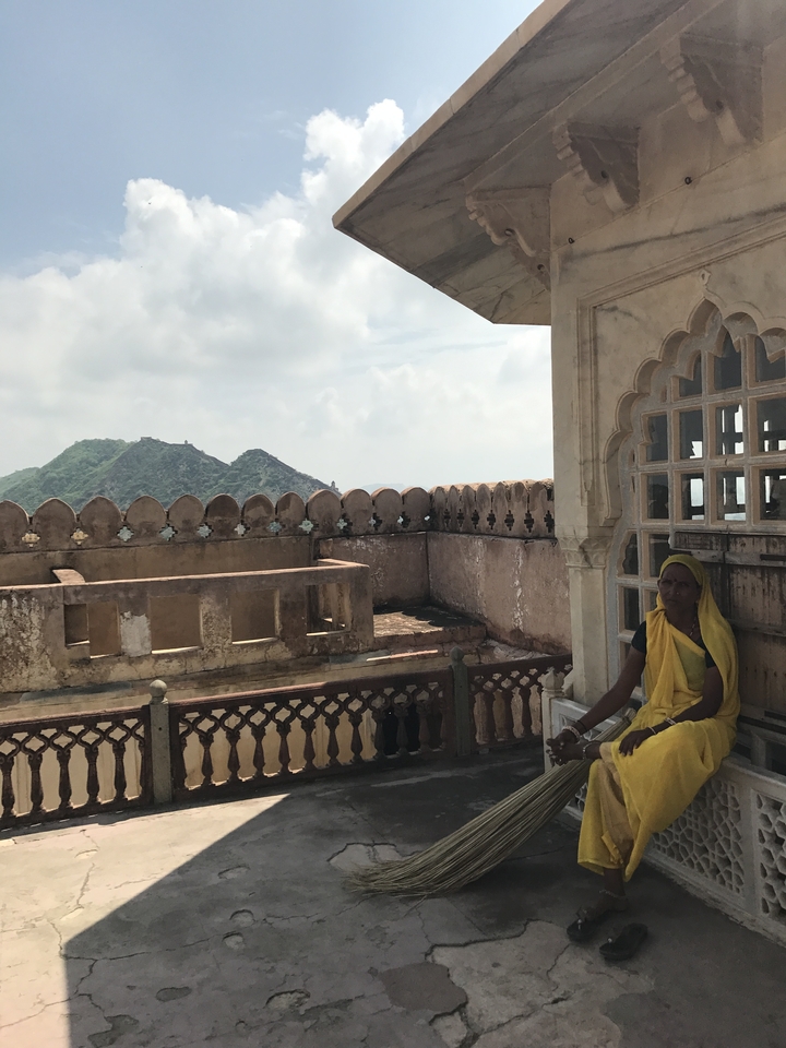 Femme assise sur un balcon historique avec des montagnes en arrière-plan.