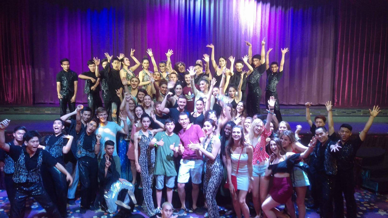 Group of performers posing on a stage with colorful lighting.