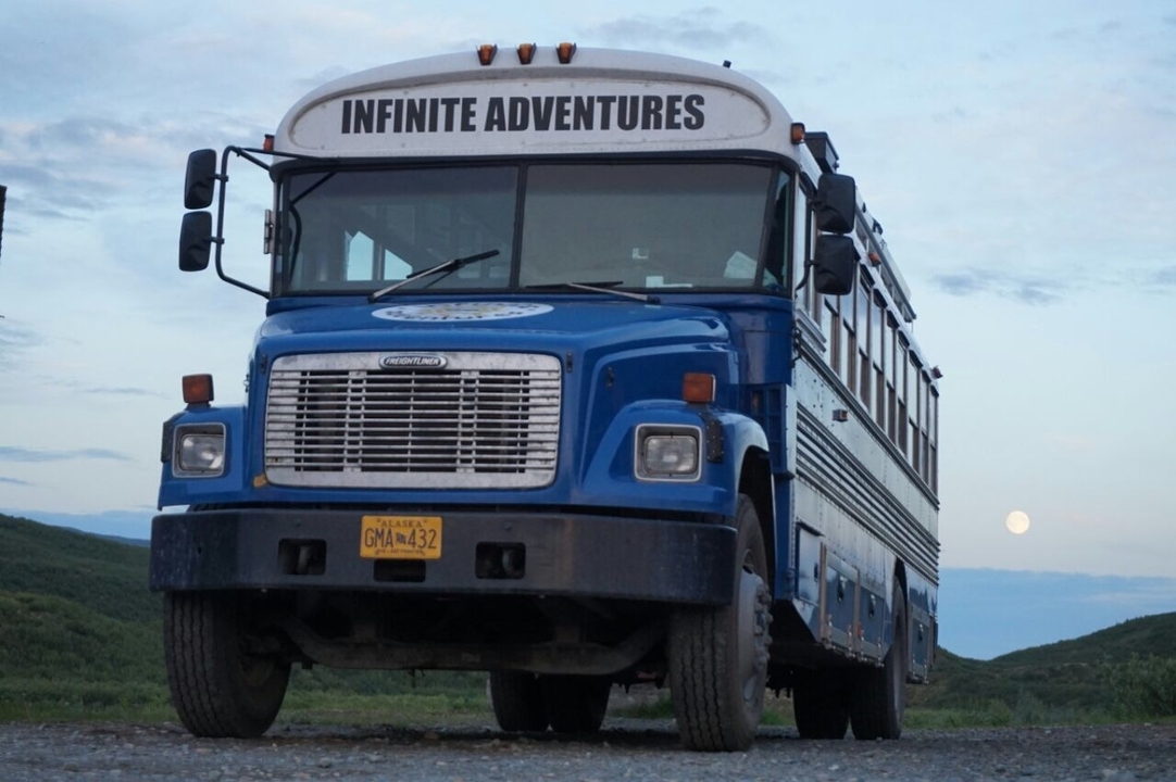 Blue adventure bus parked on a dirt road with moon visible.
