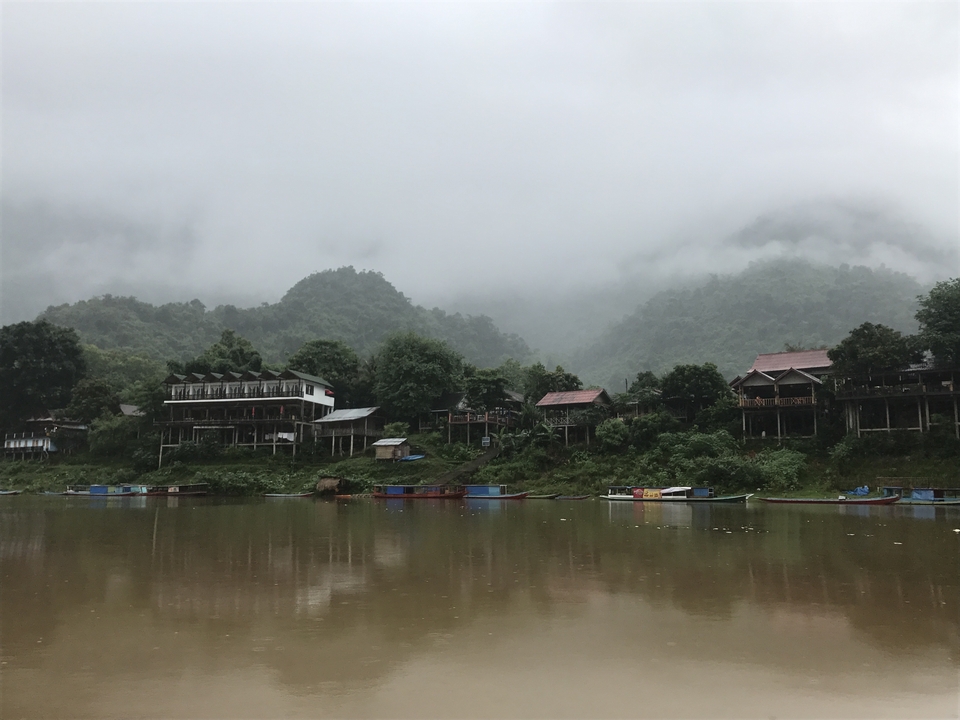 Riverside houses with misty hills in the background.