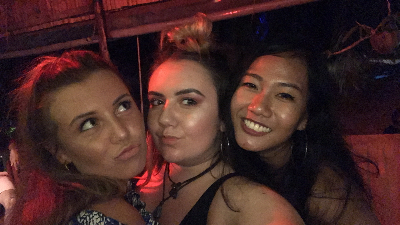 Three women posing indoors with red lighting.