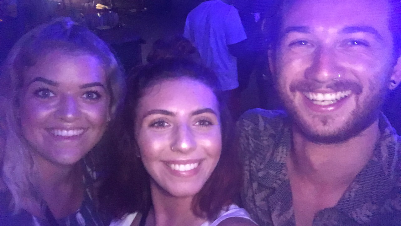 Three people smiling in a dimly lit environment.