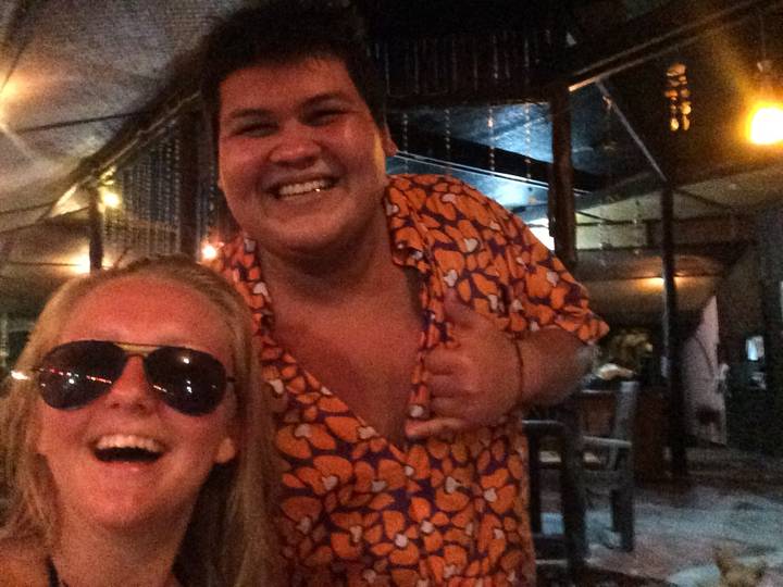 Two individuals smiling broadly in dimly lit surroundings.