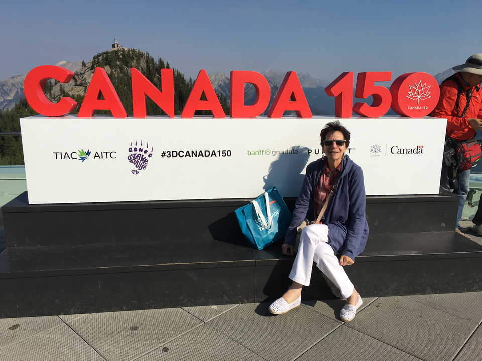 Personne profitant d'une vue près d'un panneau Canada 150 avec des montagnes.