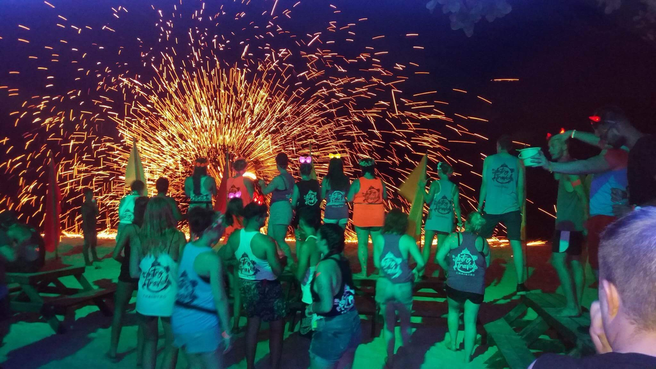 Night scene with people dancing and a fire show in the background.