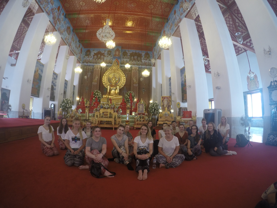 Group of people seated inside a temple with a large golden Buddha.