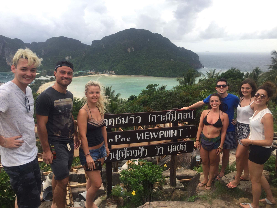 Group of travelers posing by a wooden viewpoint sign overlooking Phi Phi island bay