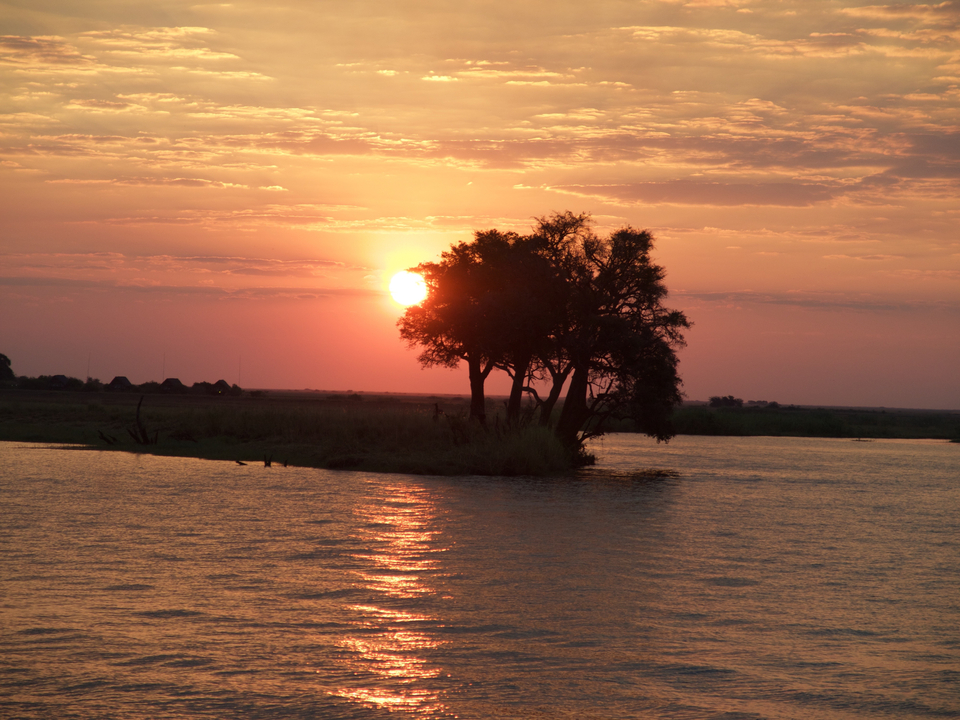 Sunset over a river with a silhouette of trees.