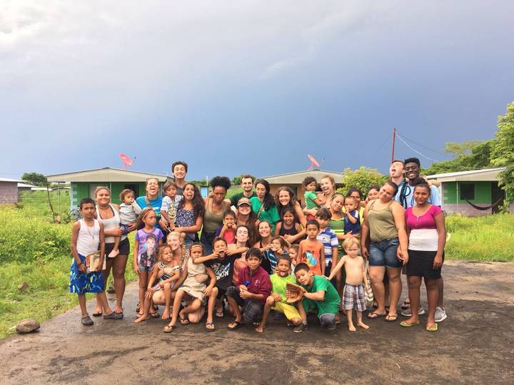 A large group of people posing outdoors with houses in the background.