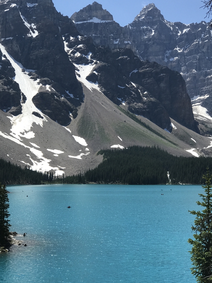 A blue lake under snowy mountains with kayaks visible.