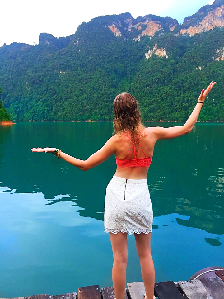 Back view of a woman standing by a scenic lake.