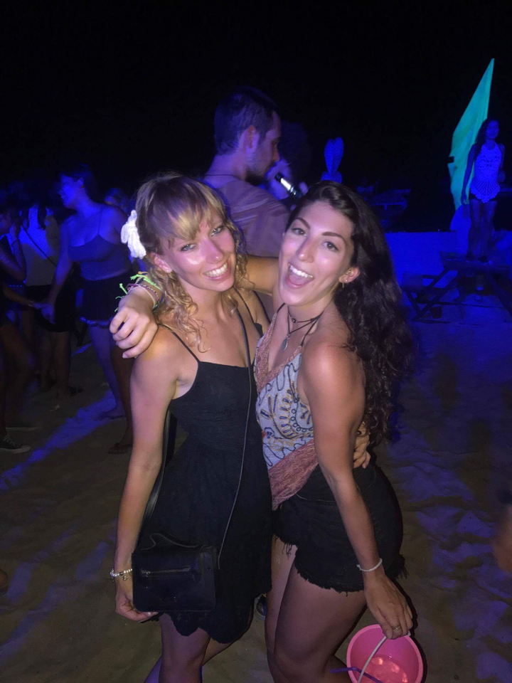 Two women posing for a photo at a night beach party.