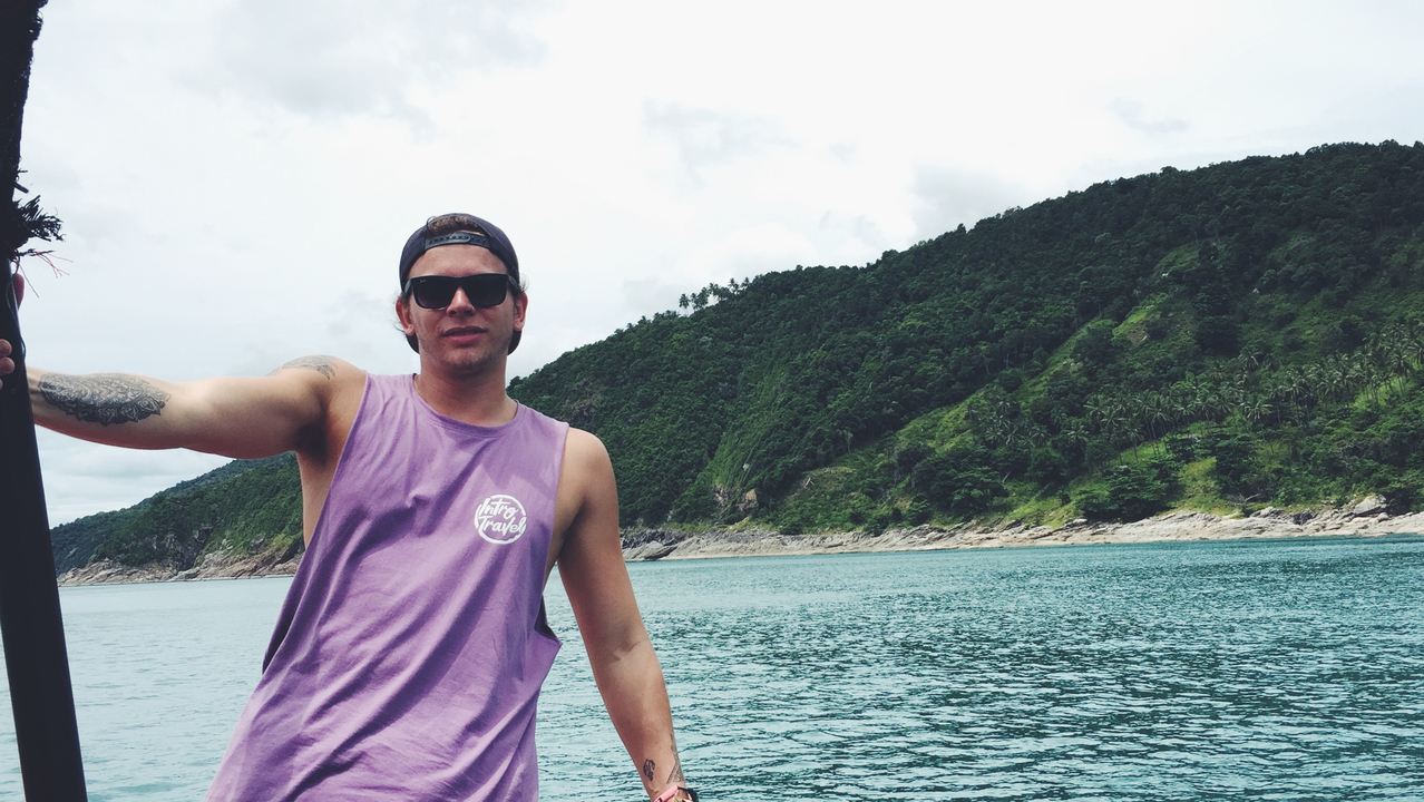 Man posing on a boat with a forested coastline in the background.