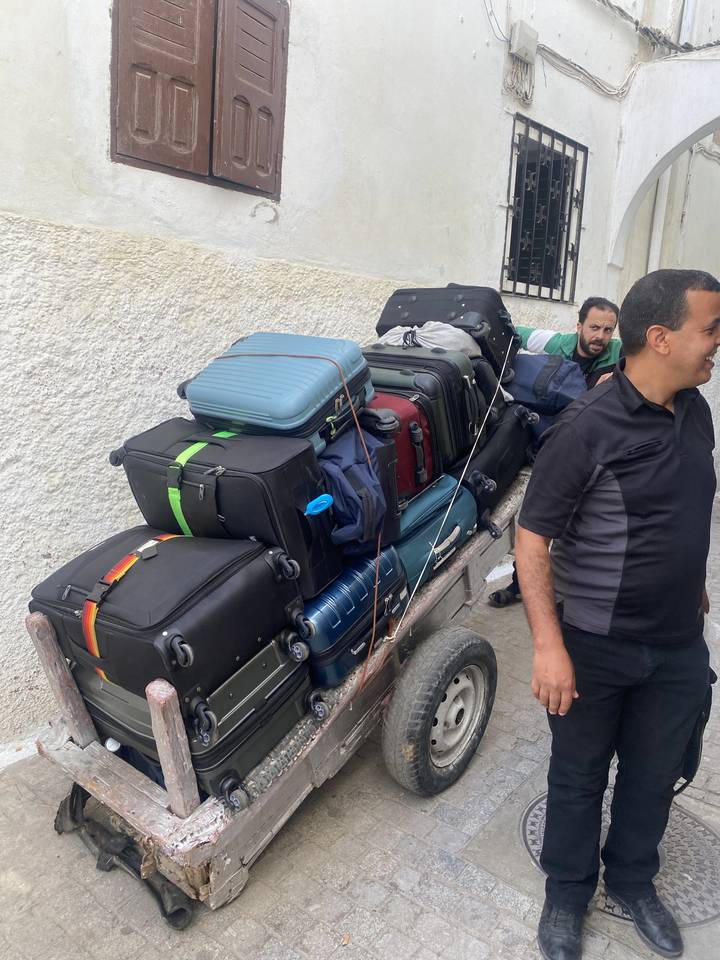 Man sitting beside a cart loaded with suitcases.