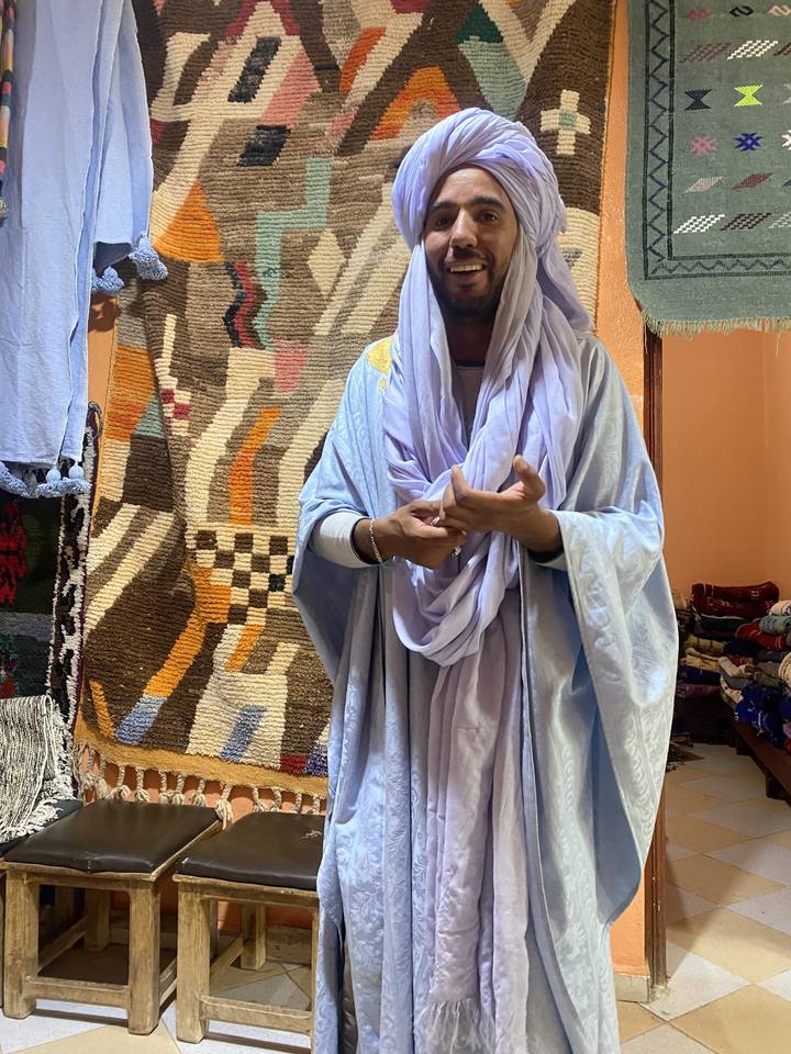 Smiling man in traditional attire inside a colorful room.