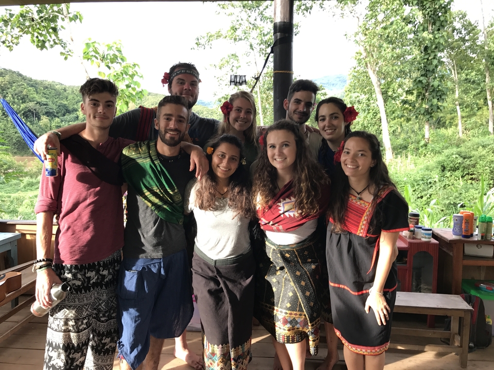 A group of people with local attire posing outdoors with foliage behind.