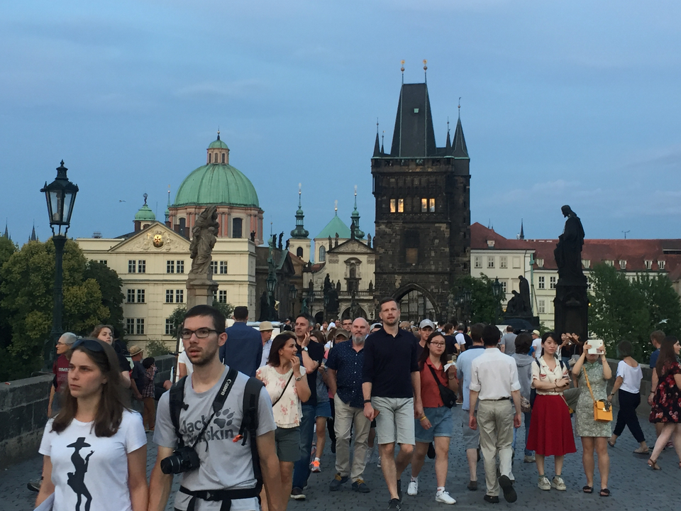 Crowd walking on a historic bridge with statues and towers.