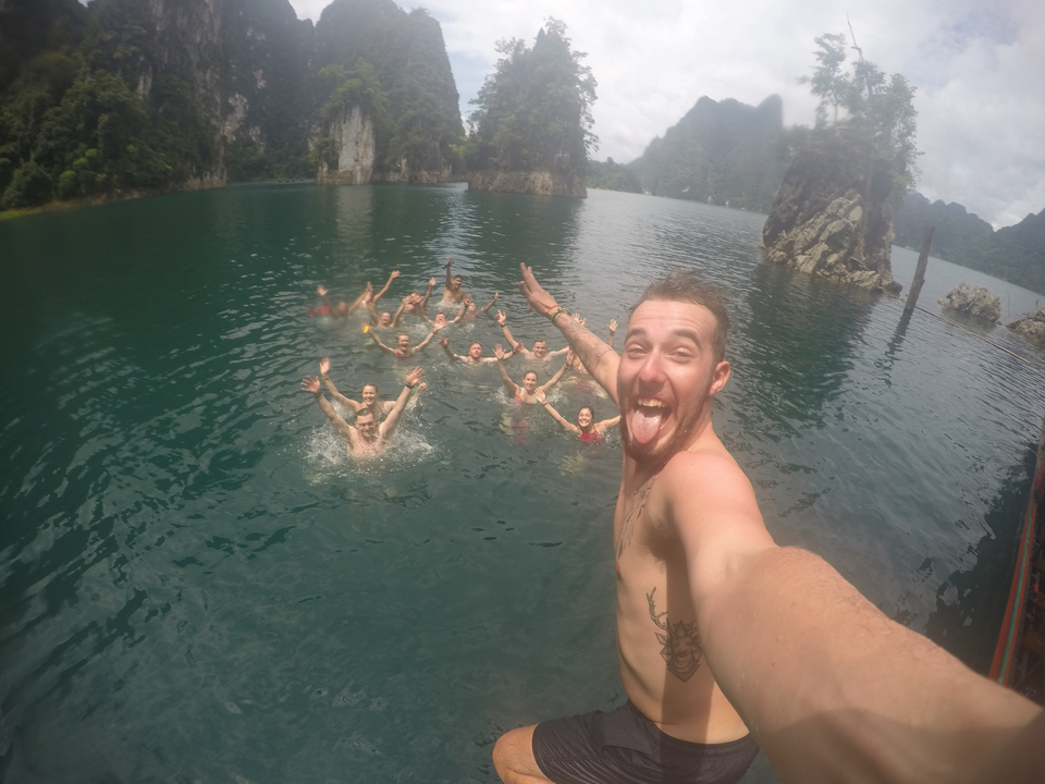 A man taking a selfie with a group of people swimming in a lake.