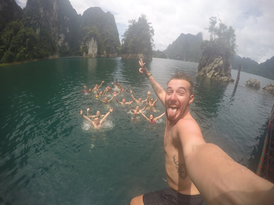 A man taking a selfie with a group of people swimming in a lake.