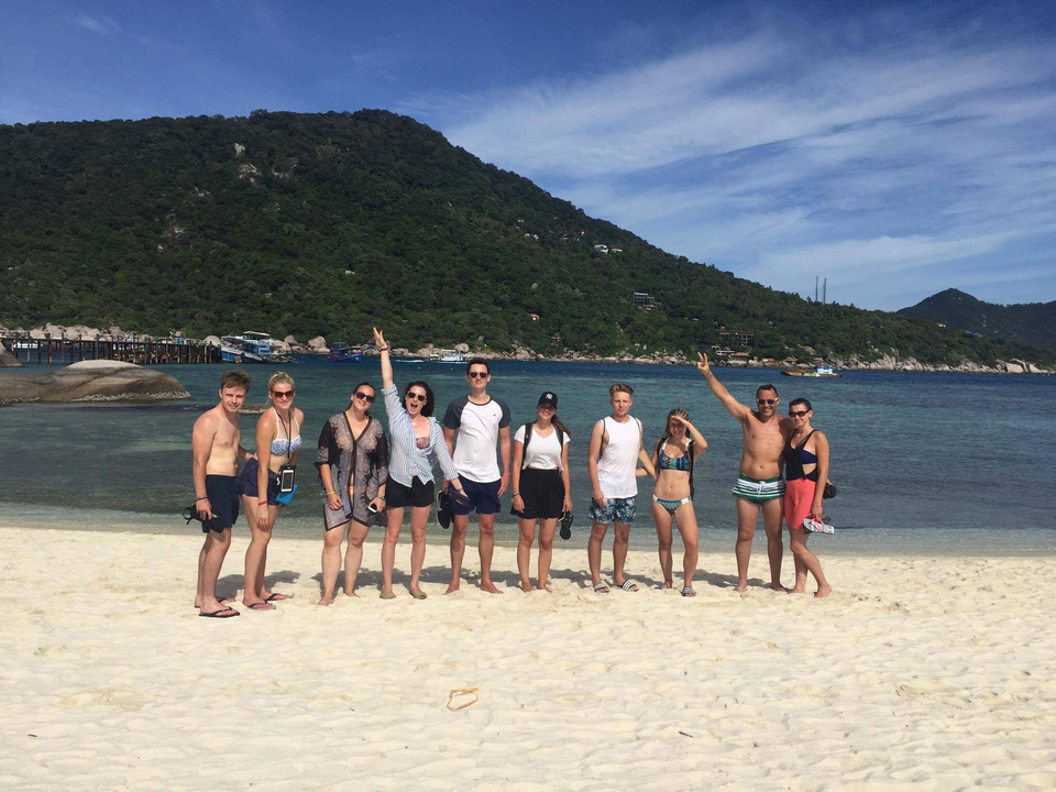 Group of people posing on a beach with distant hills.