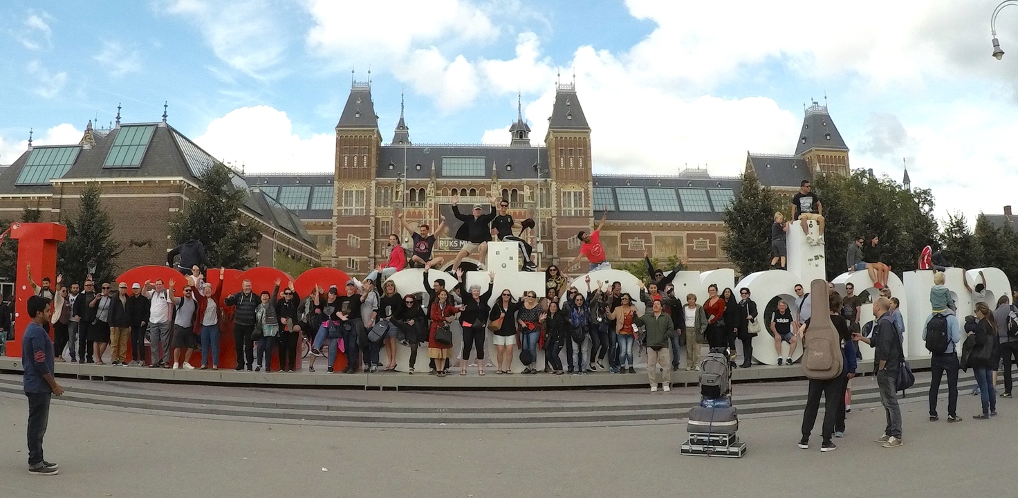 Personnes posant sur les lettres "I amsterdam" avec un musée en arrière-plan.