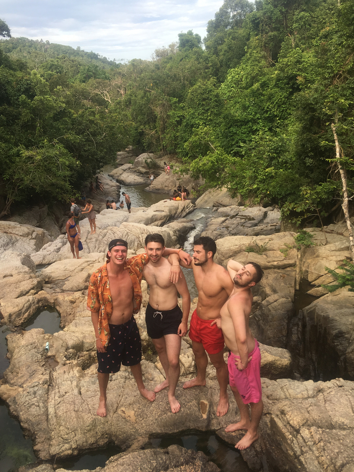 Four people standing and sitting among rocks in a natural area.