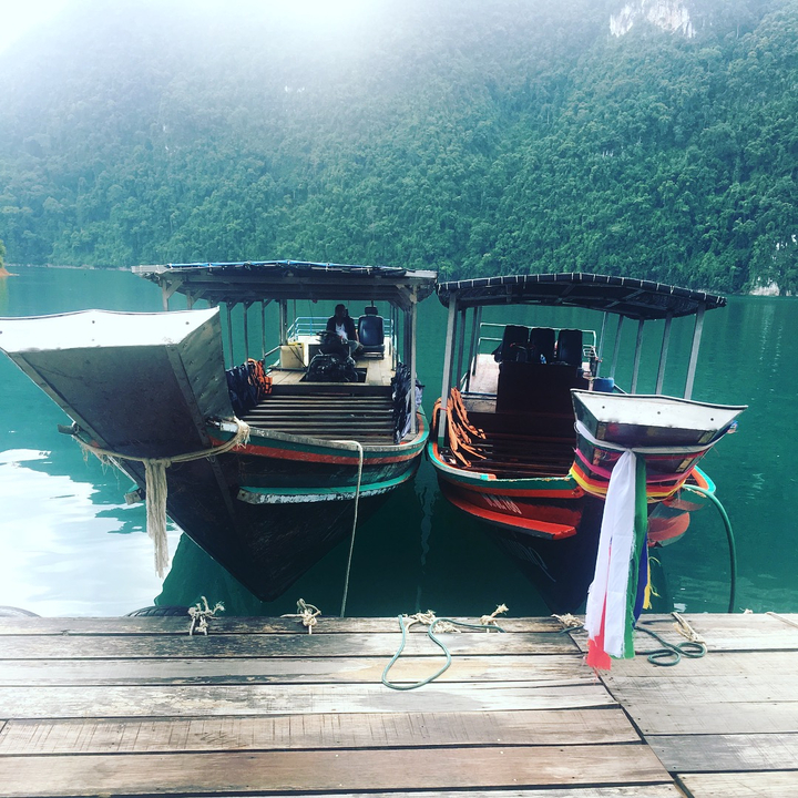 Two moored traditional boats on a calm lake surrounded by greenery.