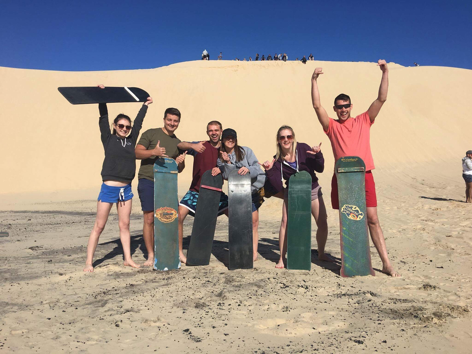 Group of people with sandboards posing on dunes.