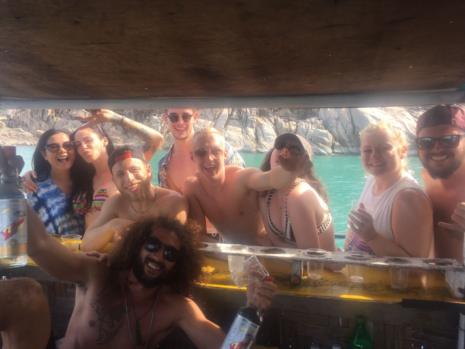 Group of people partying on a boat with shoreline in the background.