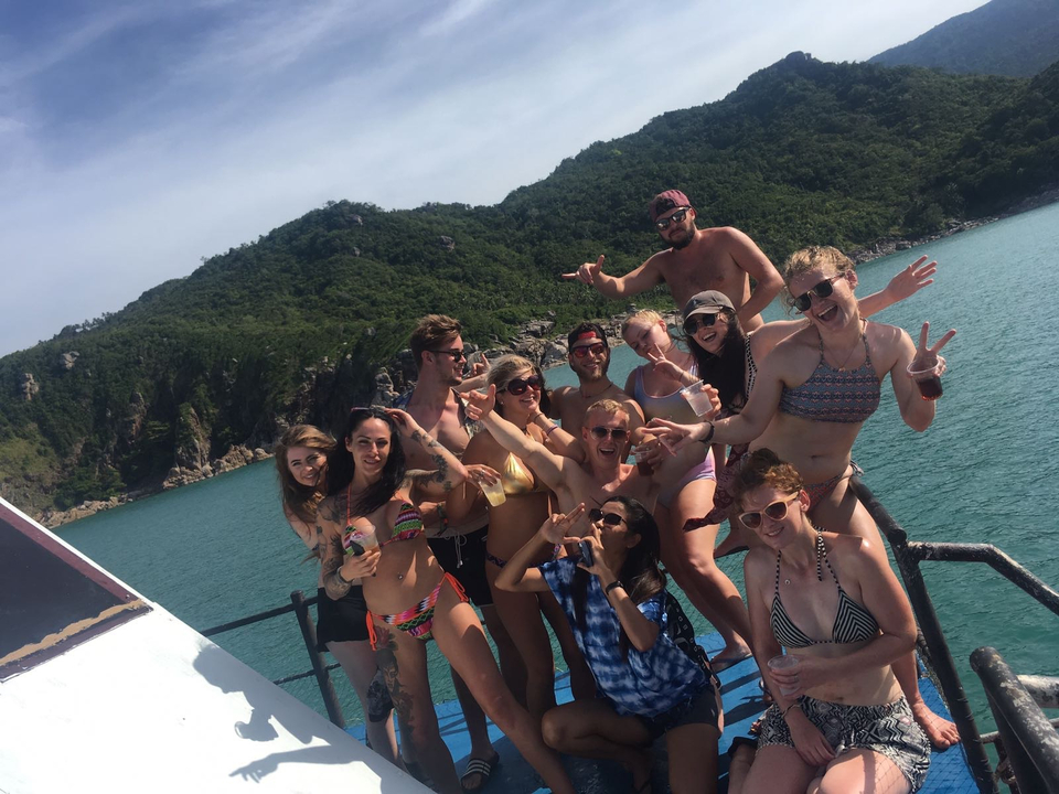 Group of people posing on a boat surrounded by green hills.