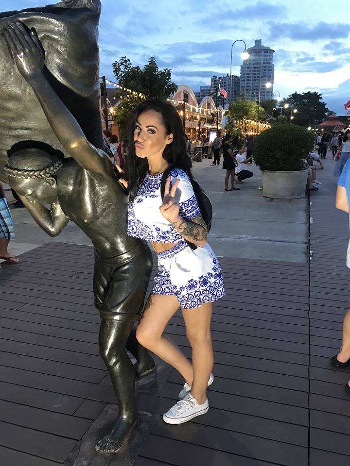 Person posing with a statue in a city street.